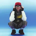 Foto von Billie Eilish, wie sie auf dem Boden hockt vor blauem Hintergrund. Foto Credits liegen bei Petros Studios
