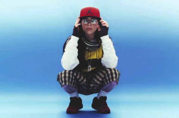 Foto von Billie Eilish, wie sie auf dem Boden hockt vor blauem Hintergrund. Foto Credits liegen bei Petros Studios
